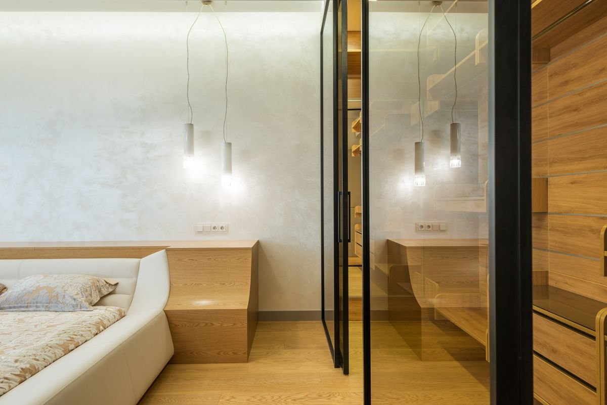 Bedroom with a walk-in wardrobe closet behind glass doors and walls, lit by LED lamps