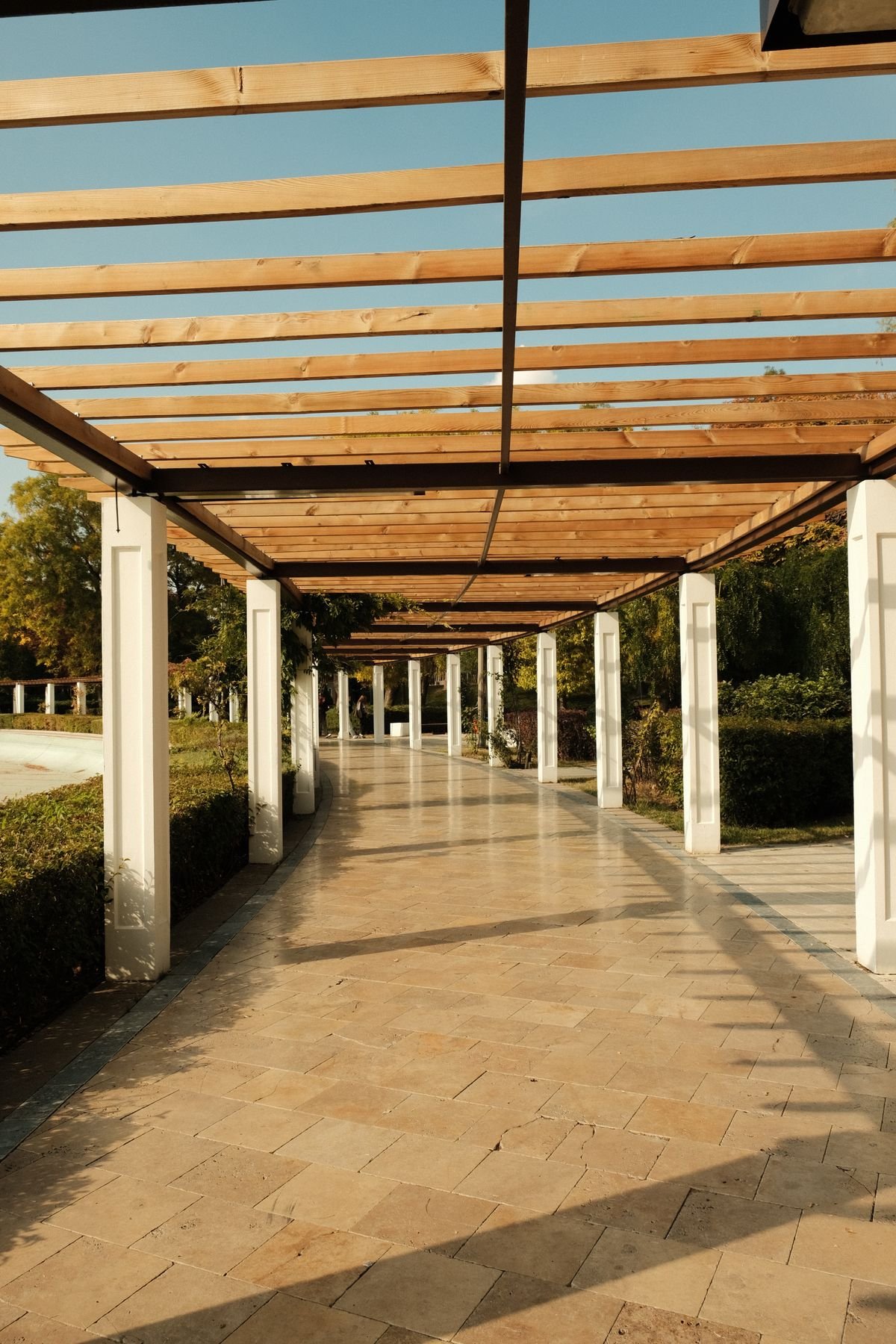 Sunlit wooden pergola forming a shaded walkway through a park with greenery on both sides