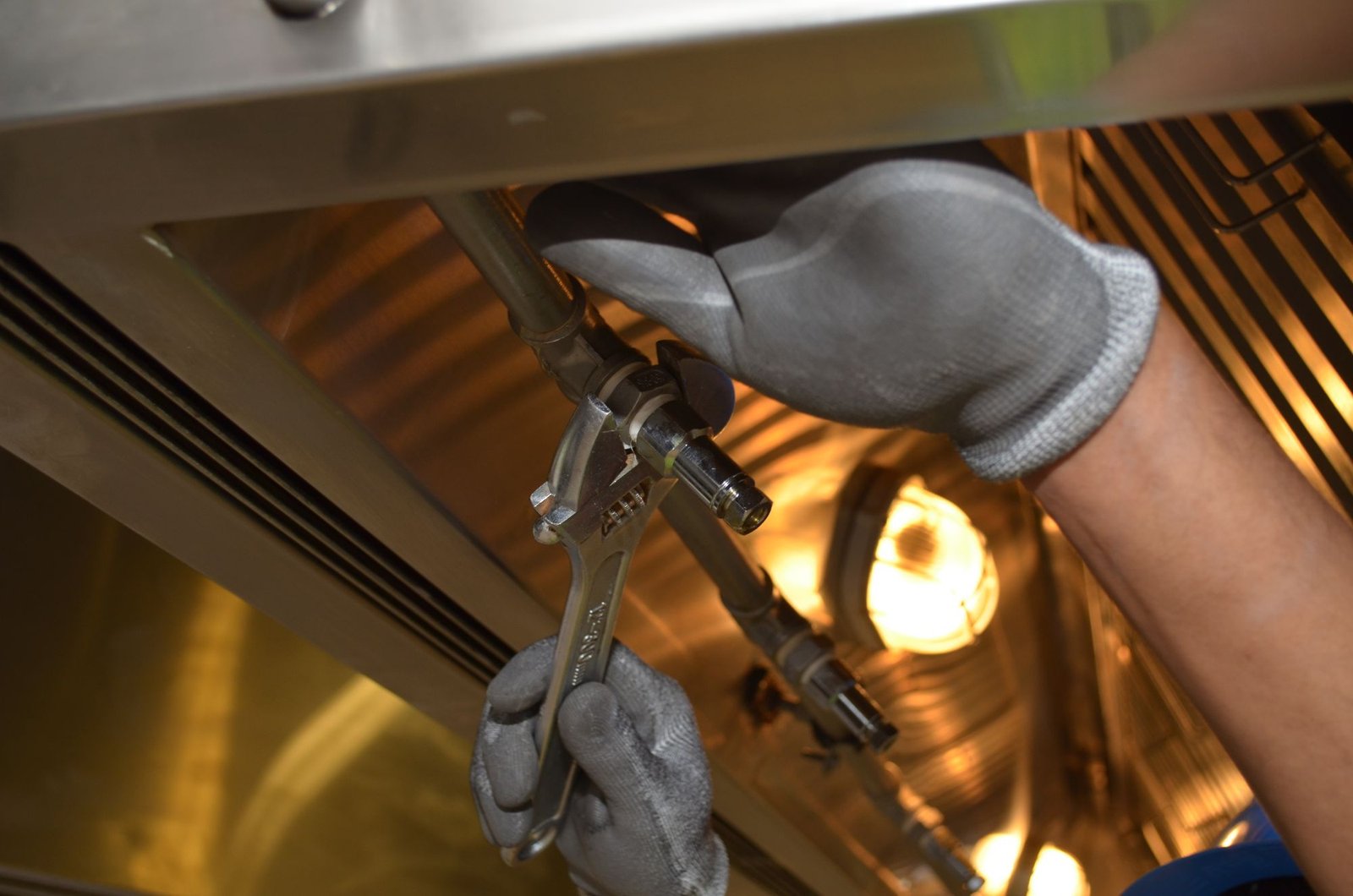 Plumber tightening a pipe fitting with a wrench under warm light