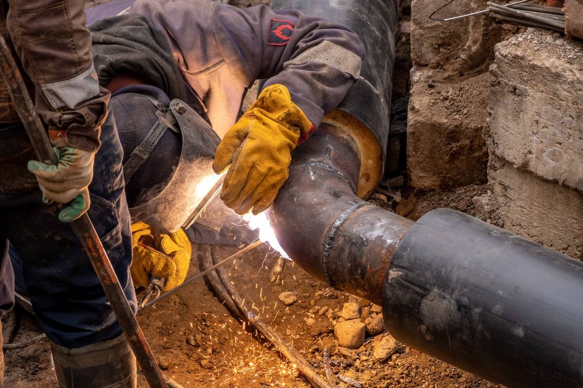Workers repairing and welding a large buried pipe