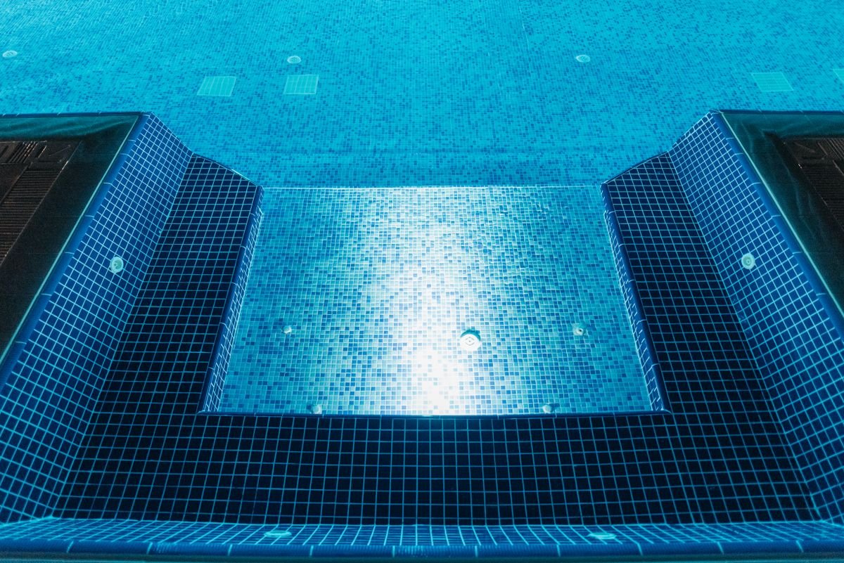 Illuminated swimming pool lined with blue and white mosaic tiles