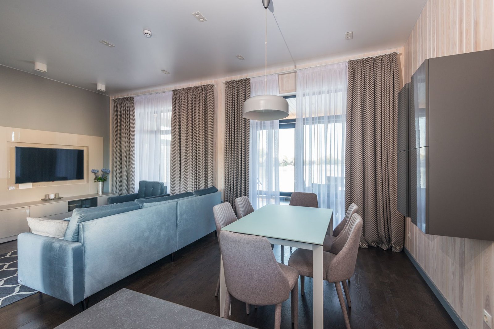 Open-plan living and dining area with a blue sofa, TV wall, and floor-length curtains
