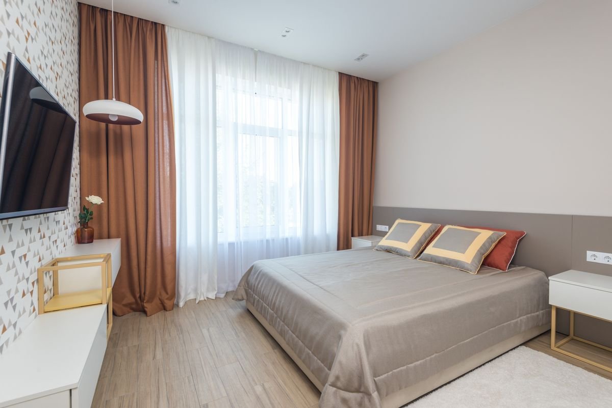 Bedroom with a beige double bed, orange curtains, and white sheers