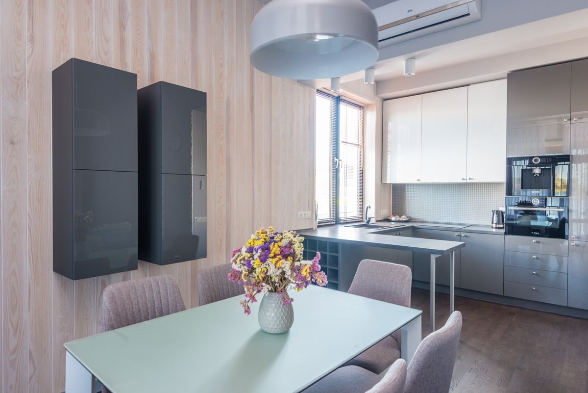 Kitchen and dining area with a pale table, fresh flowers, and dark wall cabinets