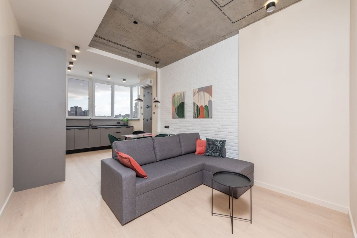Living room with a grey corner sofa, white brick feature wall, and abstract artwork