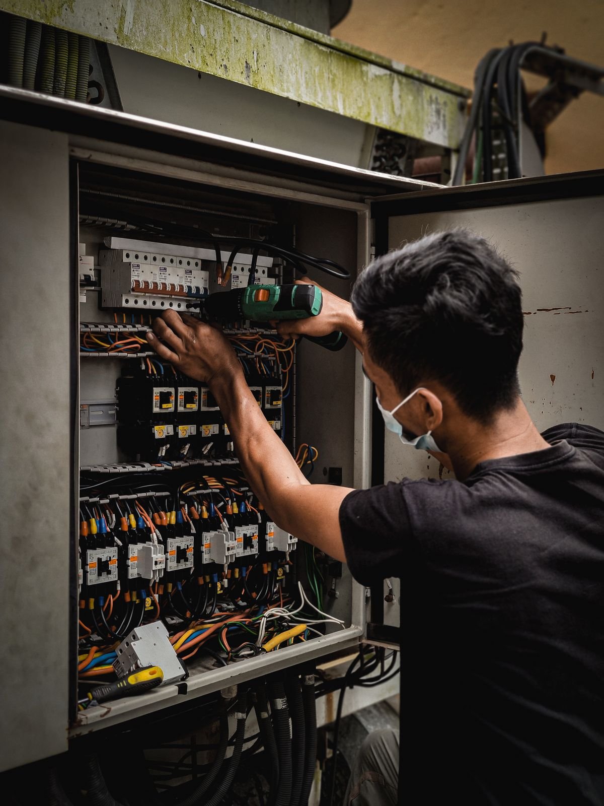 Technician working on a circuit breaker panel with a drill