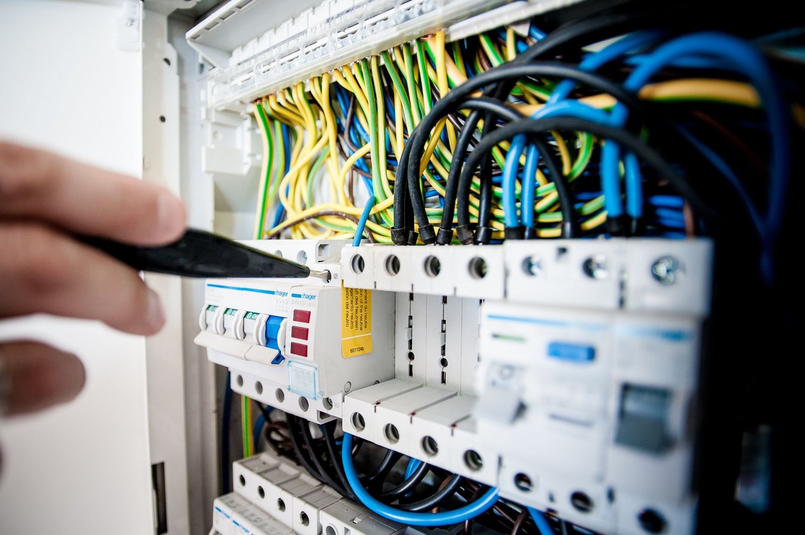 Electrician working on an open switchboard with colorful wiring, checking for a fault