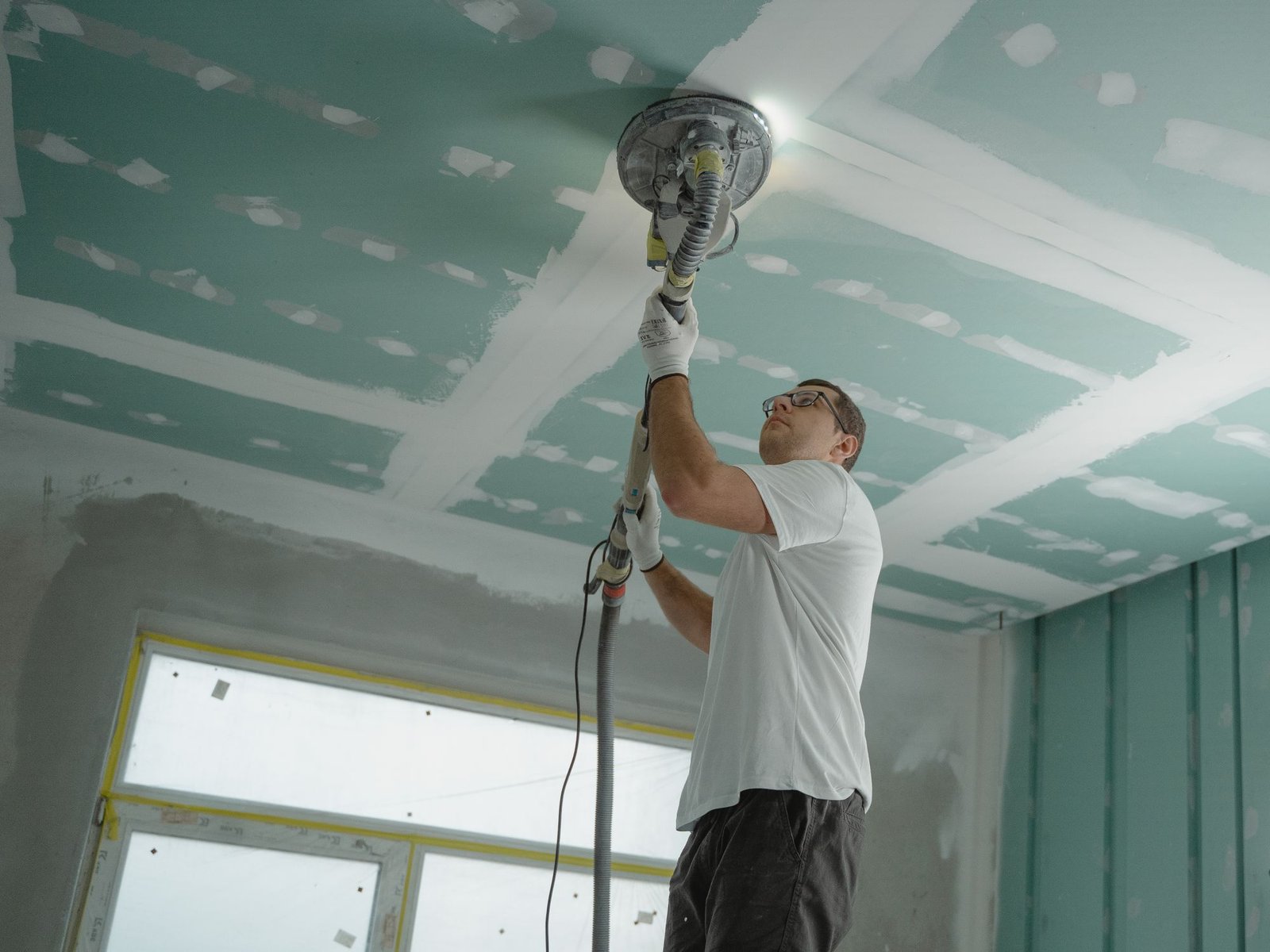 Worker sanding a freshly skim-coated ceiling smooth before painting