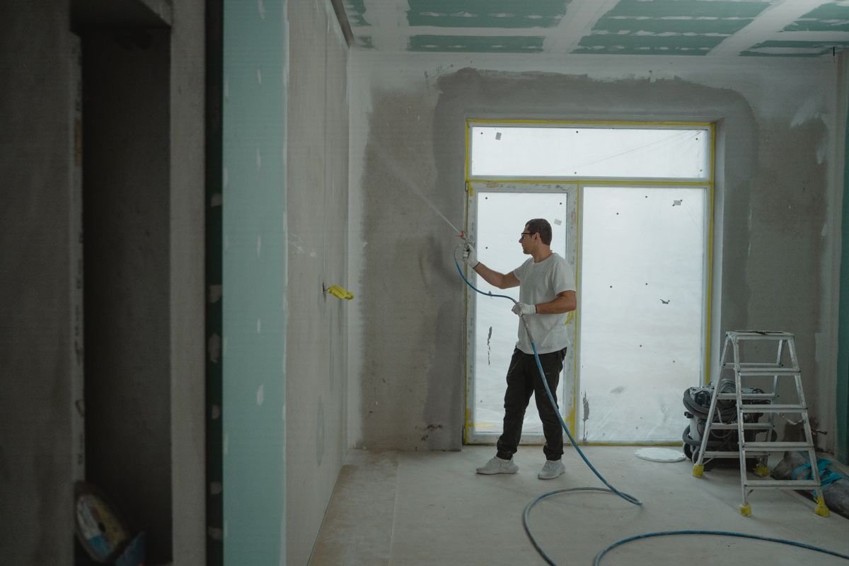Technician spray-applying a finish coat in a room under renovation