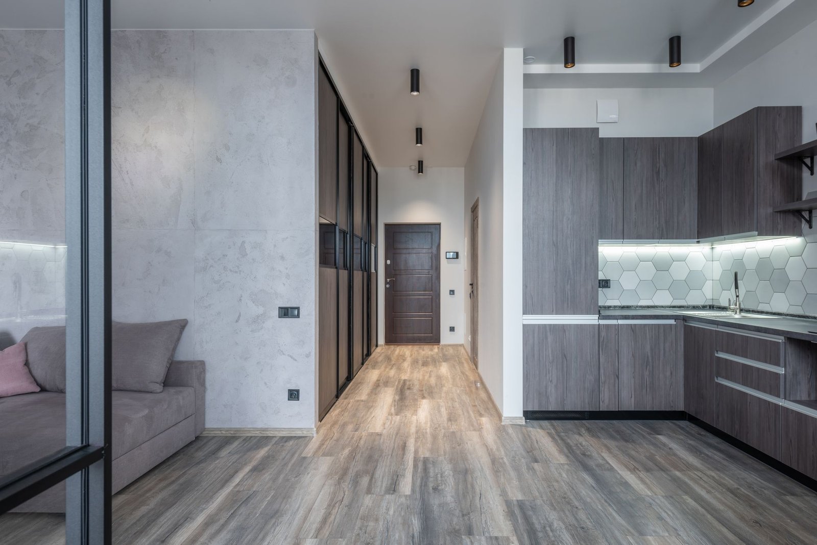 Modern apartment hallway with grey wood-look SPC flooring running into a dark kitchen