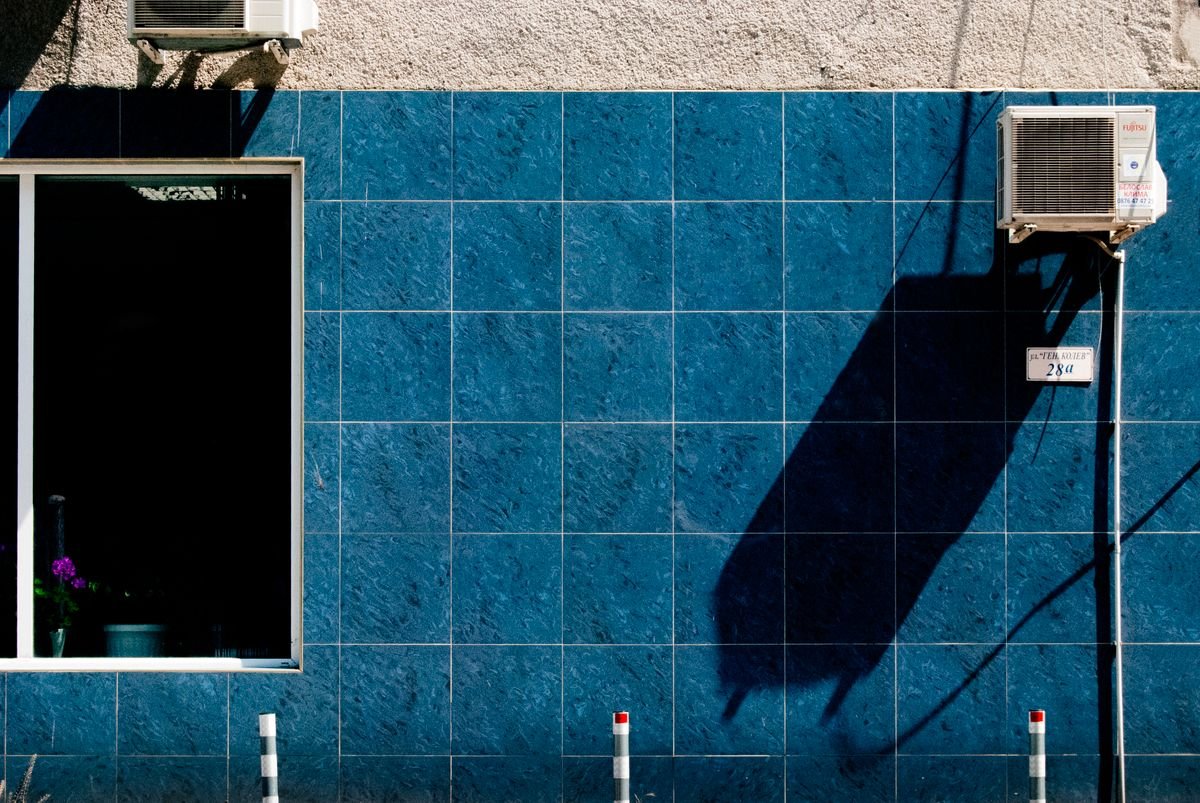 Outdoor split AC units mounted on a blue tiled urban wall