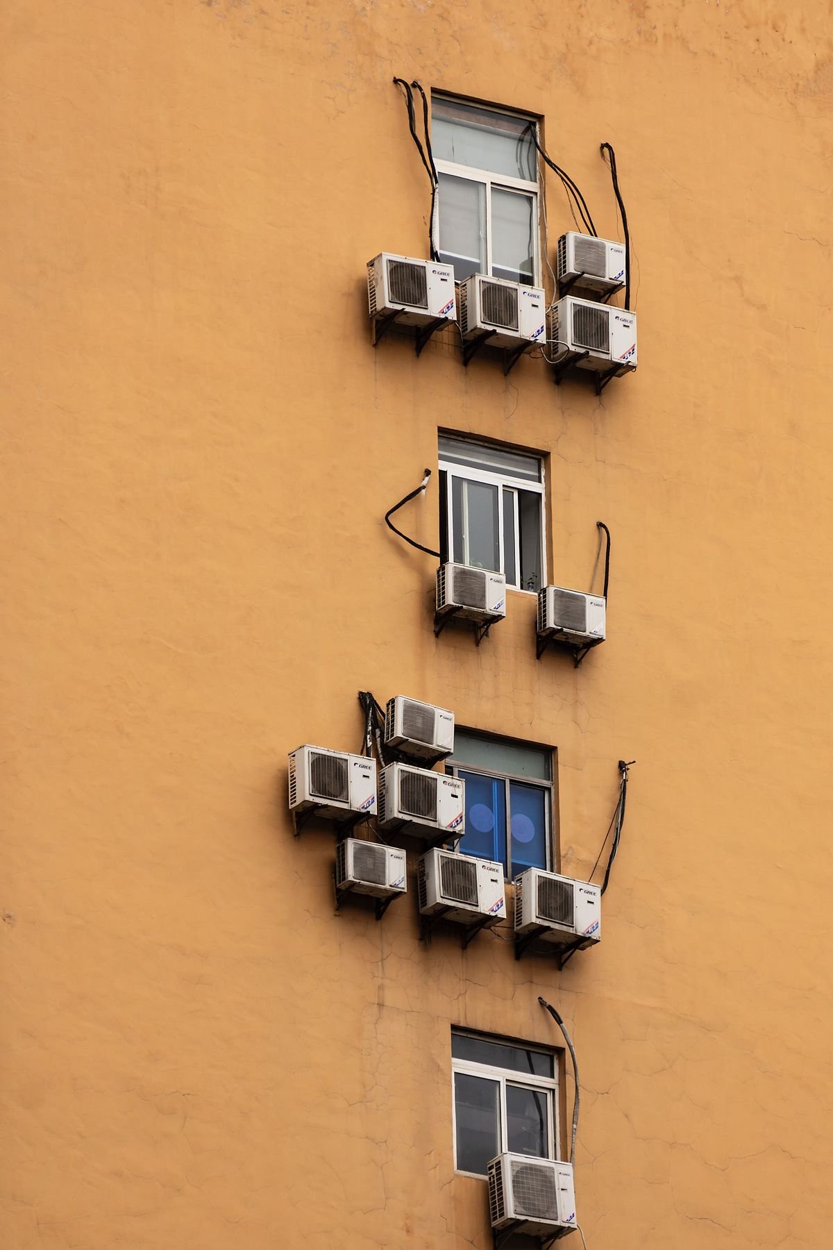 Yellow building facade with multiple outdoor split AC units attached