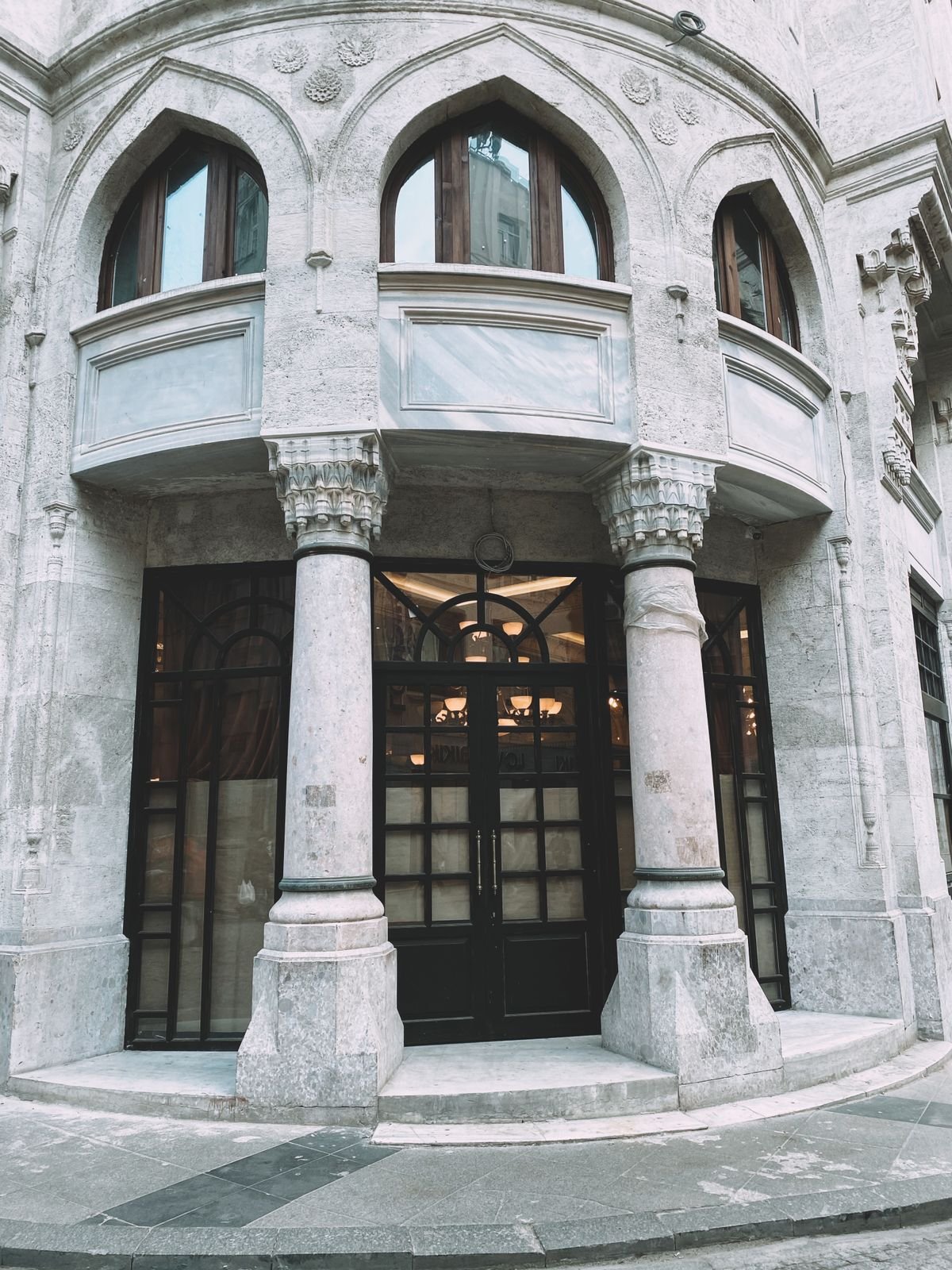 Grey concrete building with stone columns and a wooden-framed glass door