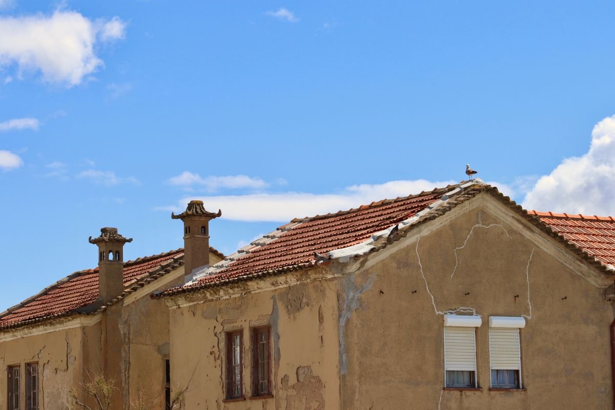 Weathered stucco facade with cracked and peeling render under a blue sky