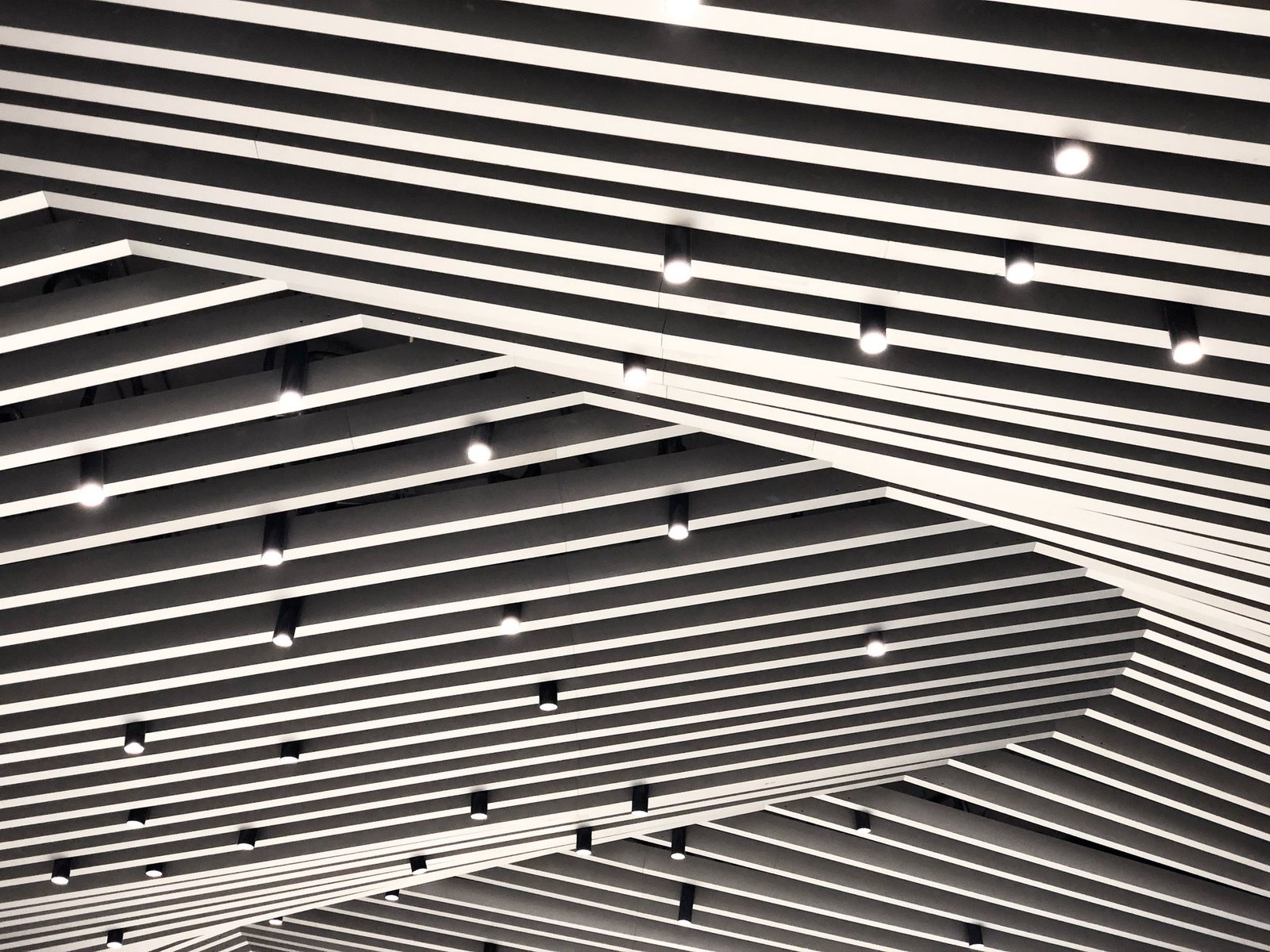 Suspended linear metal baffle ceiling with spotlights set between the slats