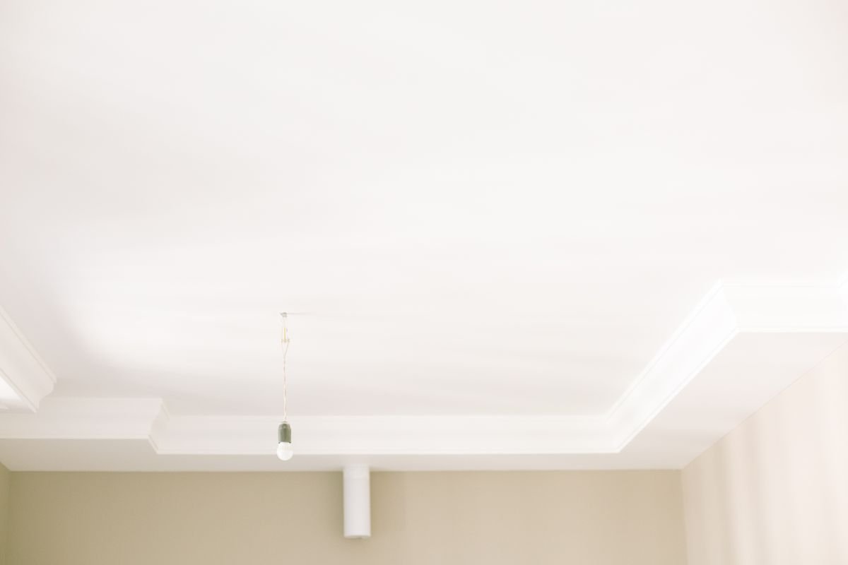 Plain white ceiling with a cornice and single hanging bulb before new works