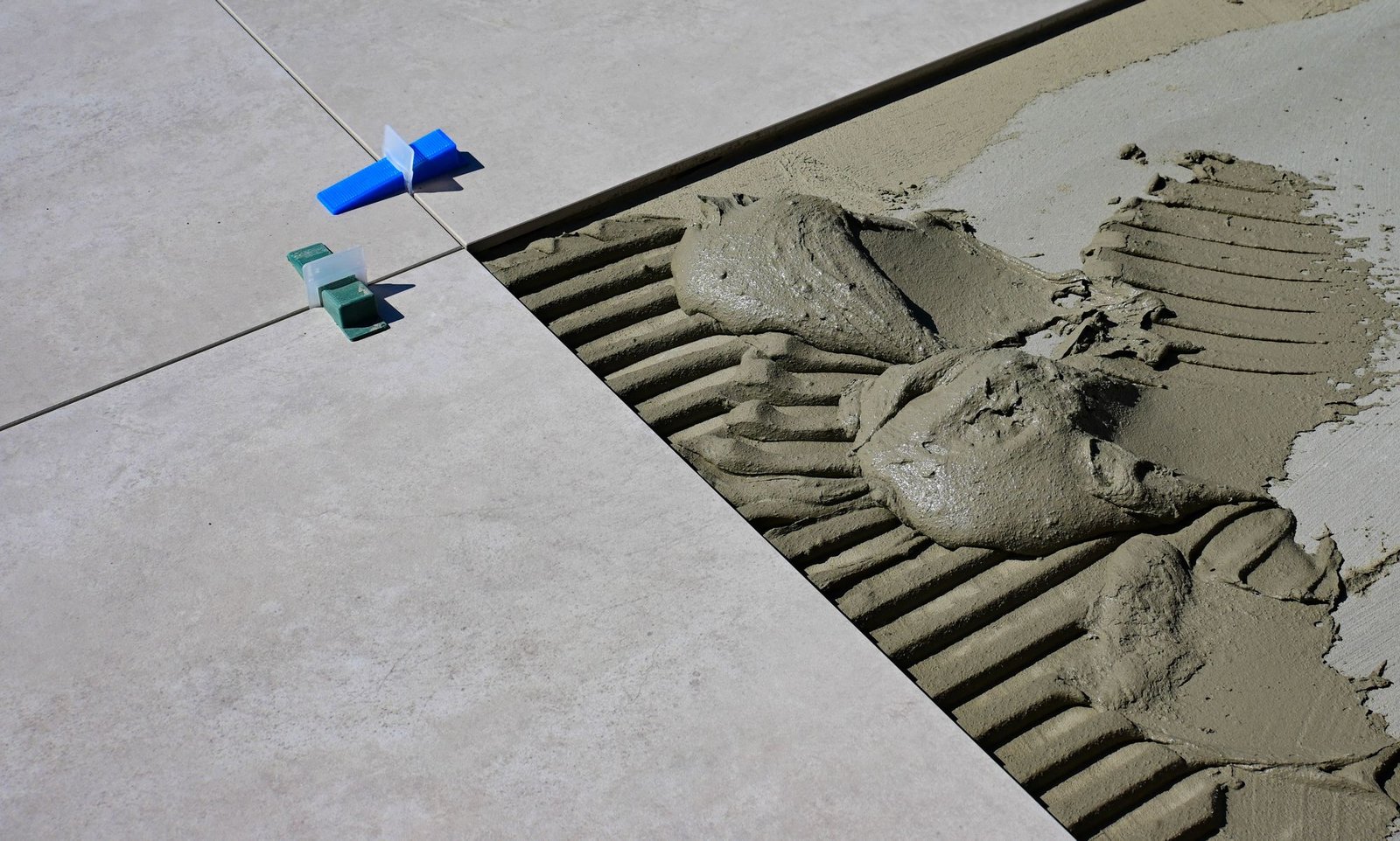 Adhesive and blue levelling clips beside a large porcelain tile on a job site