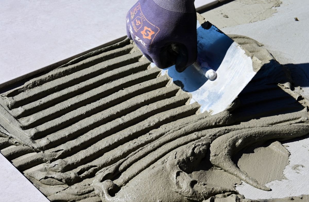 Trowel scooping pale adhesive from ridged bedding on a floor