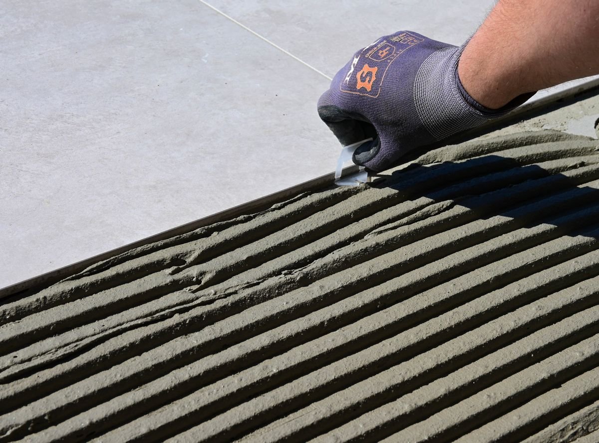 Gloved hand next to combed adhesive ridges and a large porcelain tile