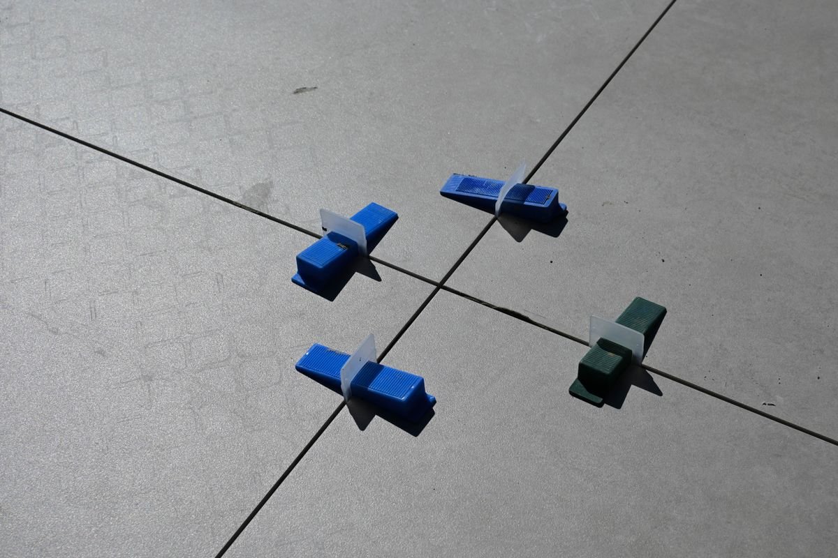 Blue and green levelling clips set at the corner of four large floor tiles