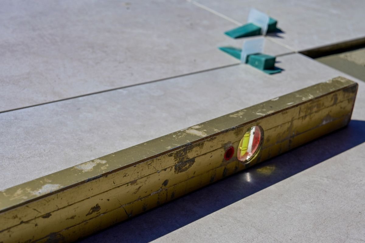Spirit level resting across large floor tiles to check they are flat