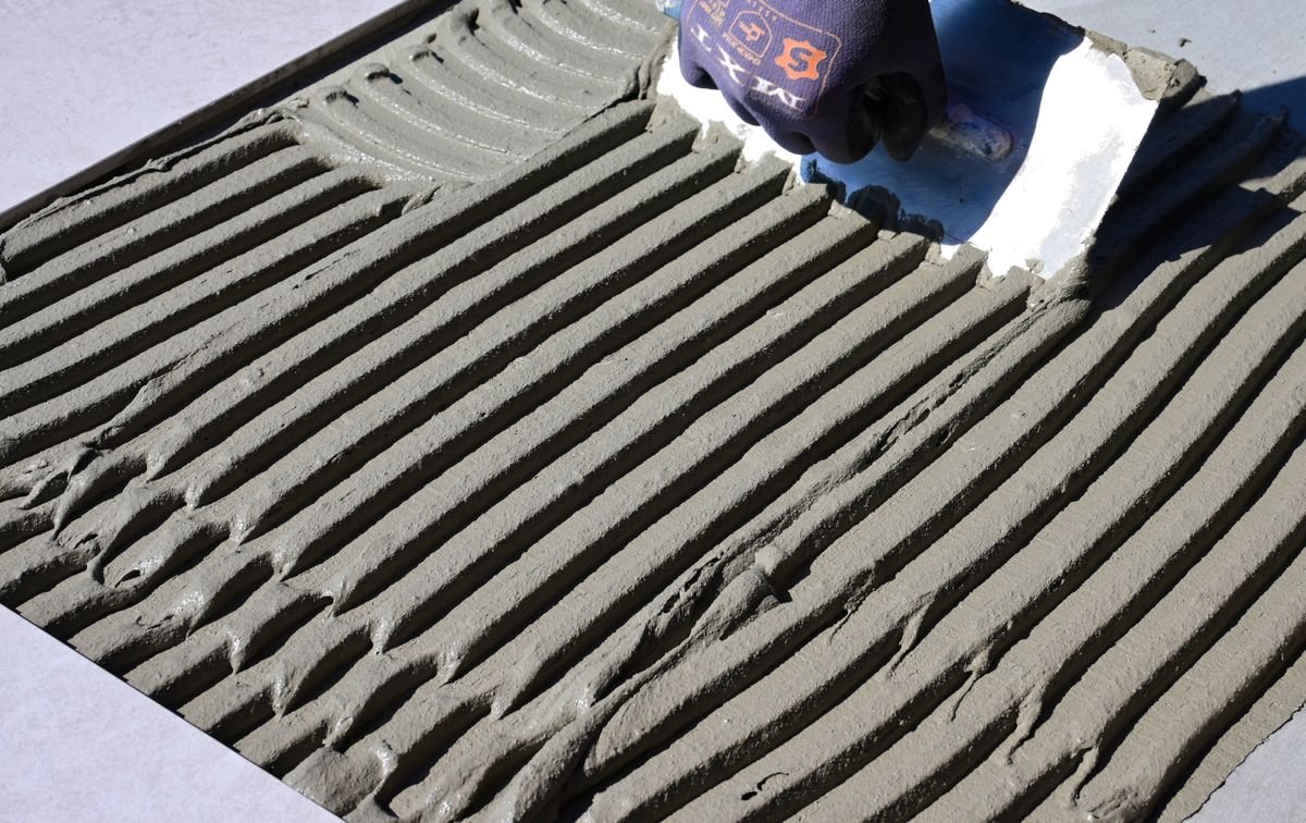 Gloved hand drawing a trowel across ridged tile adhesive