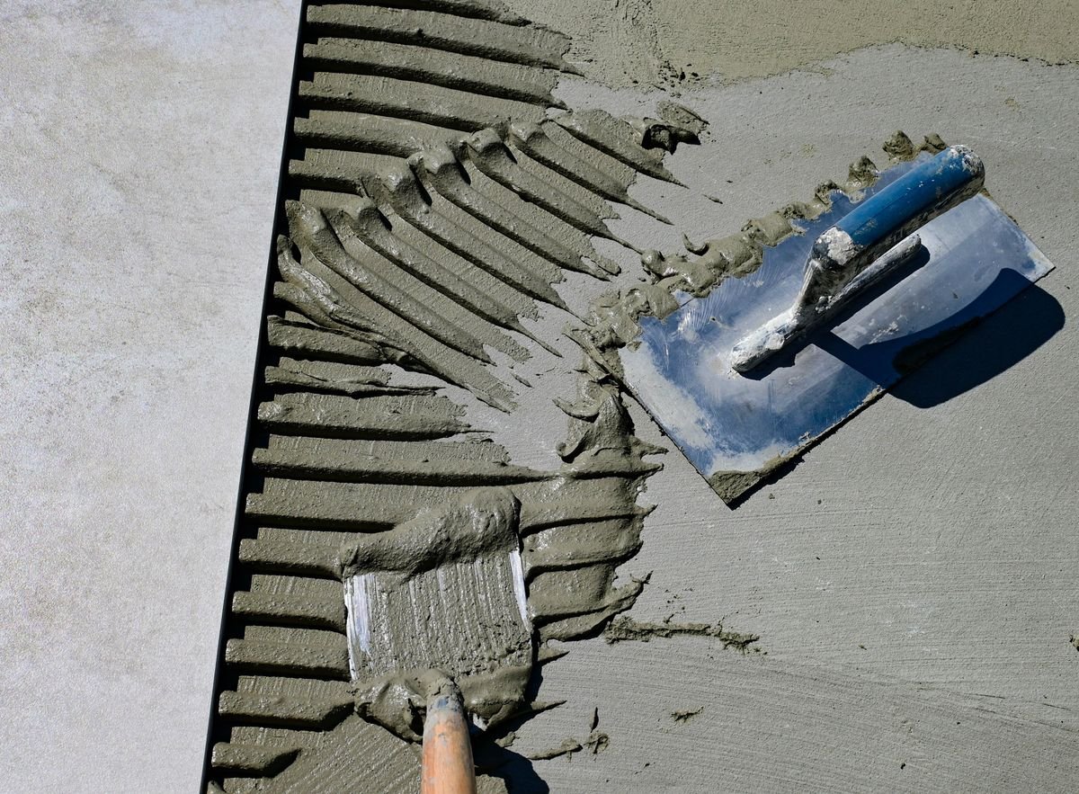 Trowel resting in ridged adhesive on a floor ready for tiles
