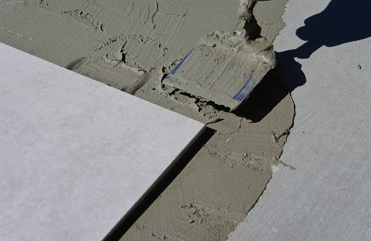 Adhesive being spread with a trowel next to a laid porcelain tile
