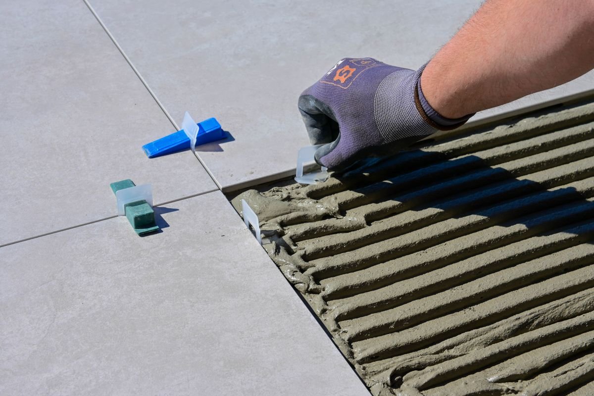 Gloved hand placing a levelling clip beside trowelled adhesive