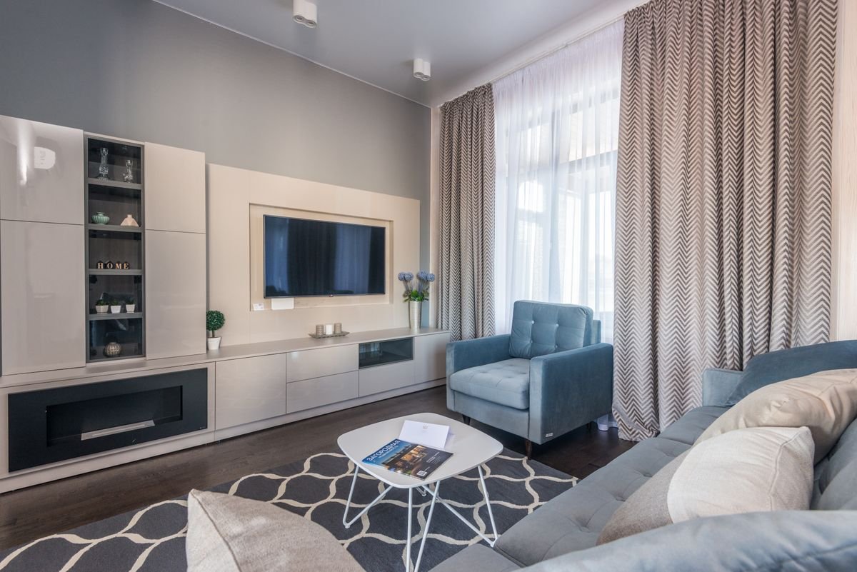 Living room with a built-in TV wall, linear fireplace, blue armchair, and patterned rug