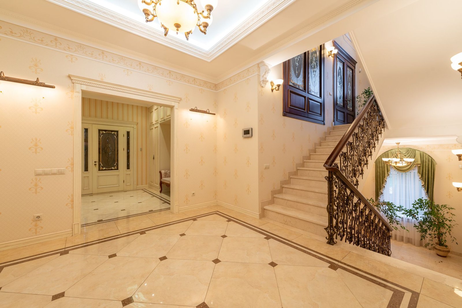 Villa entrance hall with a grand staircase, gold chandelier, and cream marble floor