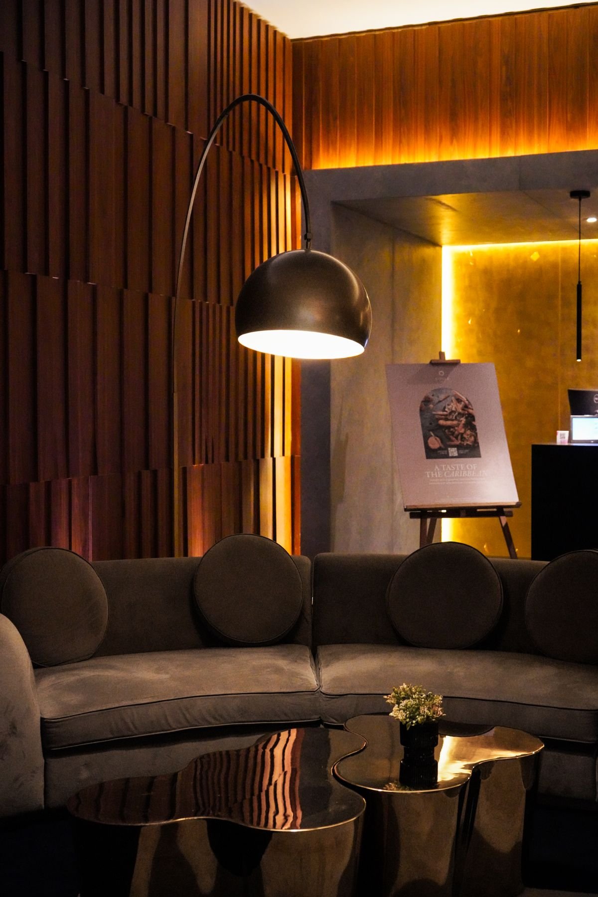 Warmly lit lounge with a curved sofa, arc floor lamp, and timber wall panelling