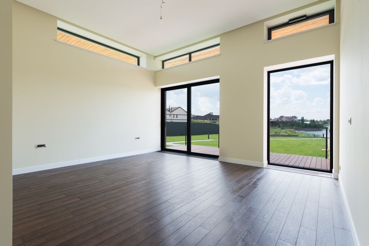 Spacious empty villa room with cream painted walls and floor-to-ceiling glass doors