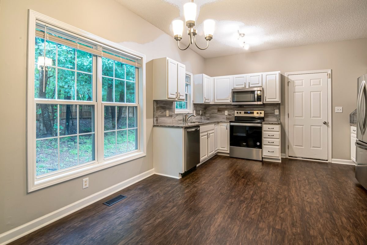 Kitchen with white cabinets, a large window, and a dark wood-look vinyl floor