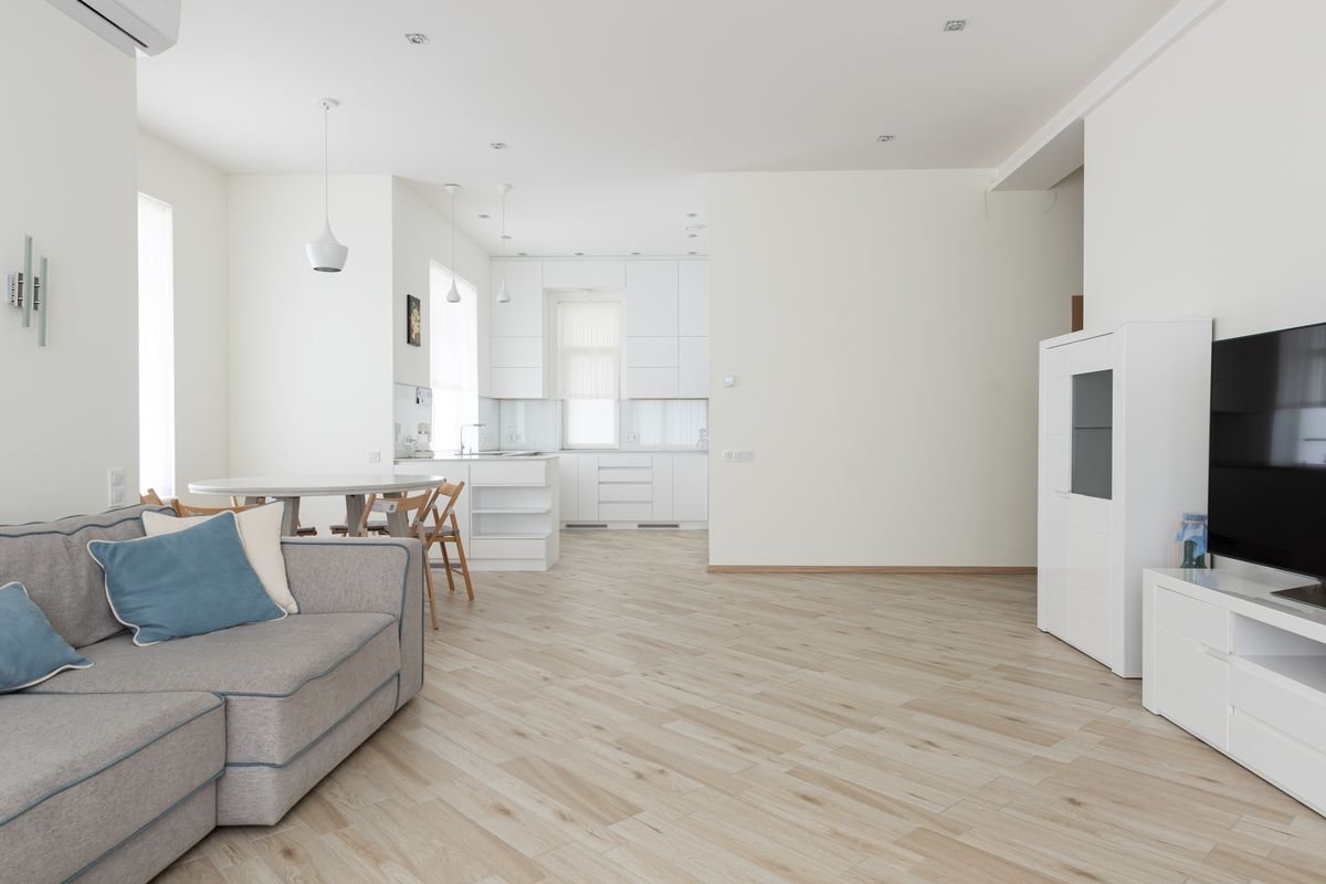 Open-plan living and kitchen area with pale grey wood-look flooring and a corner sofa