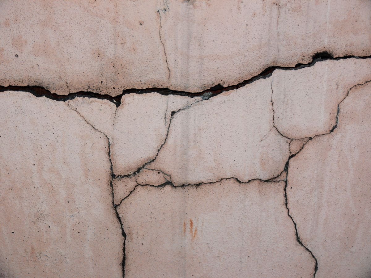 Network of cracks spreading across a beige plaster wall