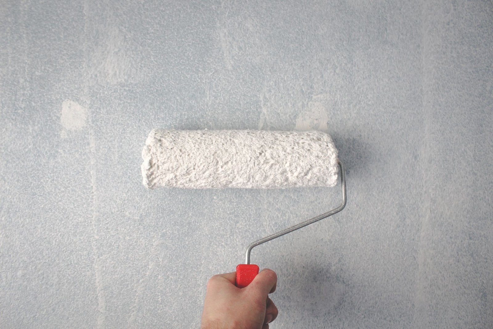 Hand using a paint roller to apply fresh white paint over a blue-grey wall
