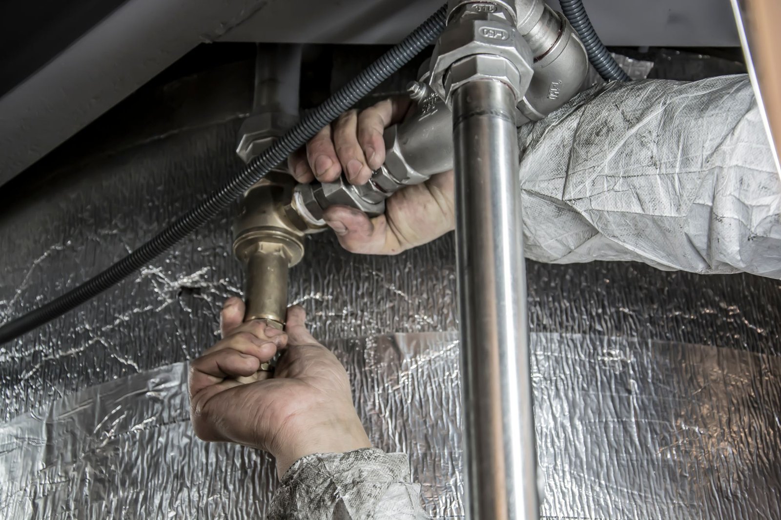Technician hands fitting pipe connections near an insulated water heater tank
