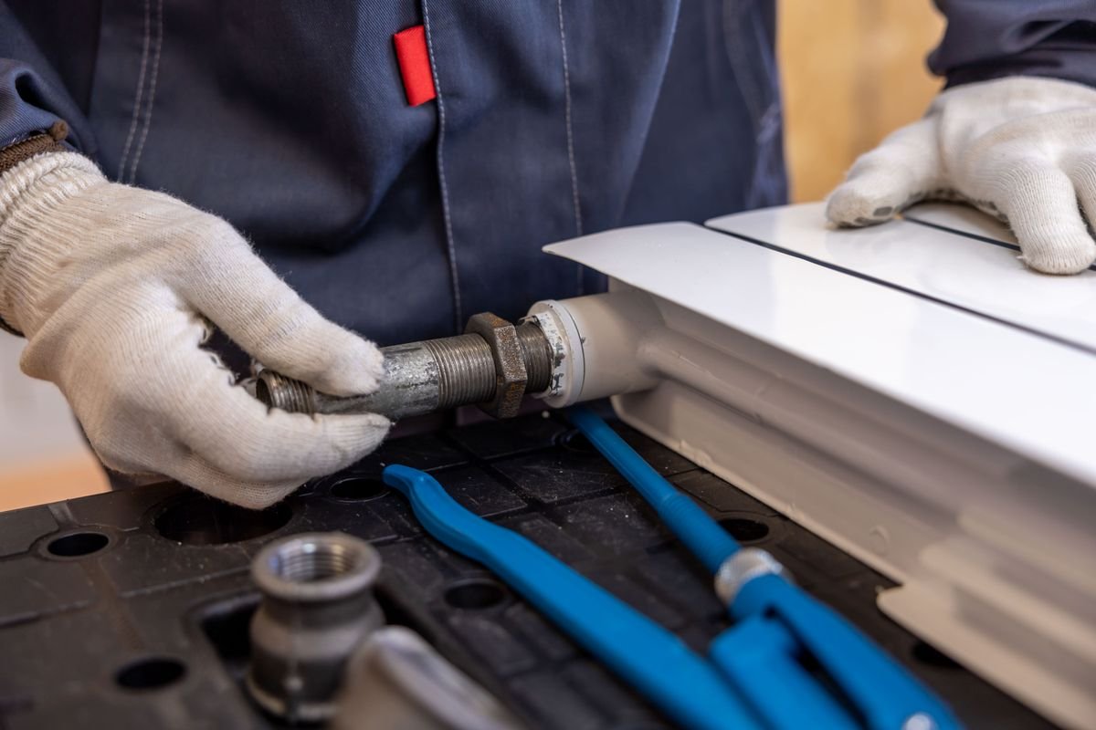 Gloved hands installing a pipe fitting on a heating radiator