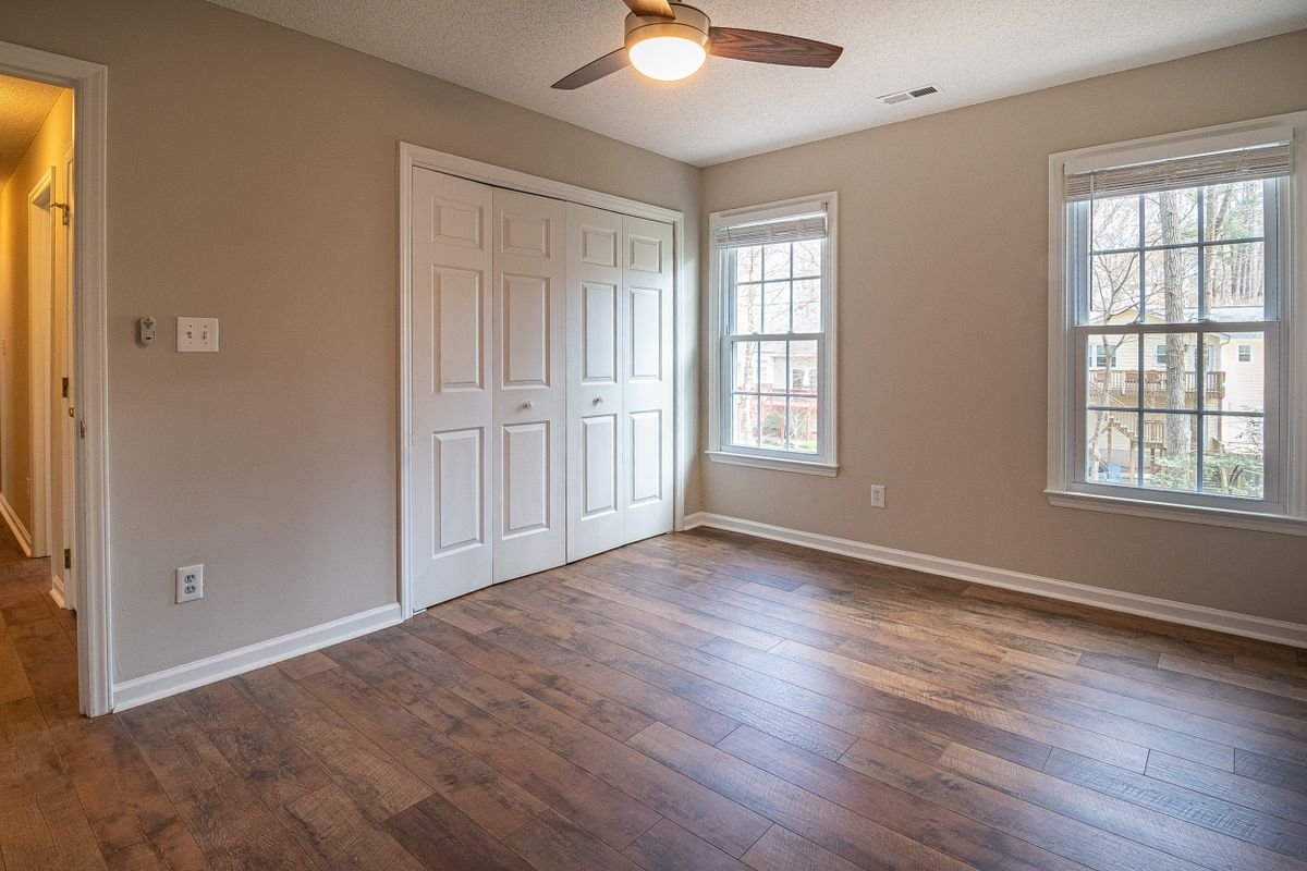 Empty room with hardwood floors, a ceiling fan, and natural light from the windows