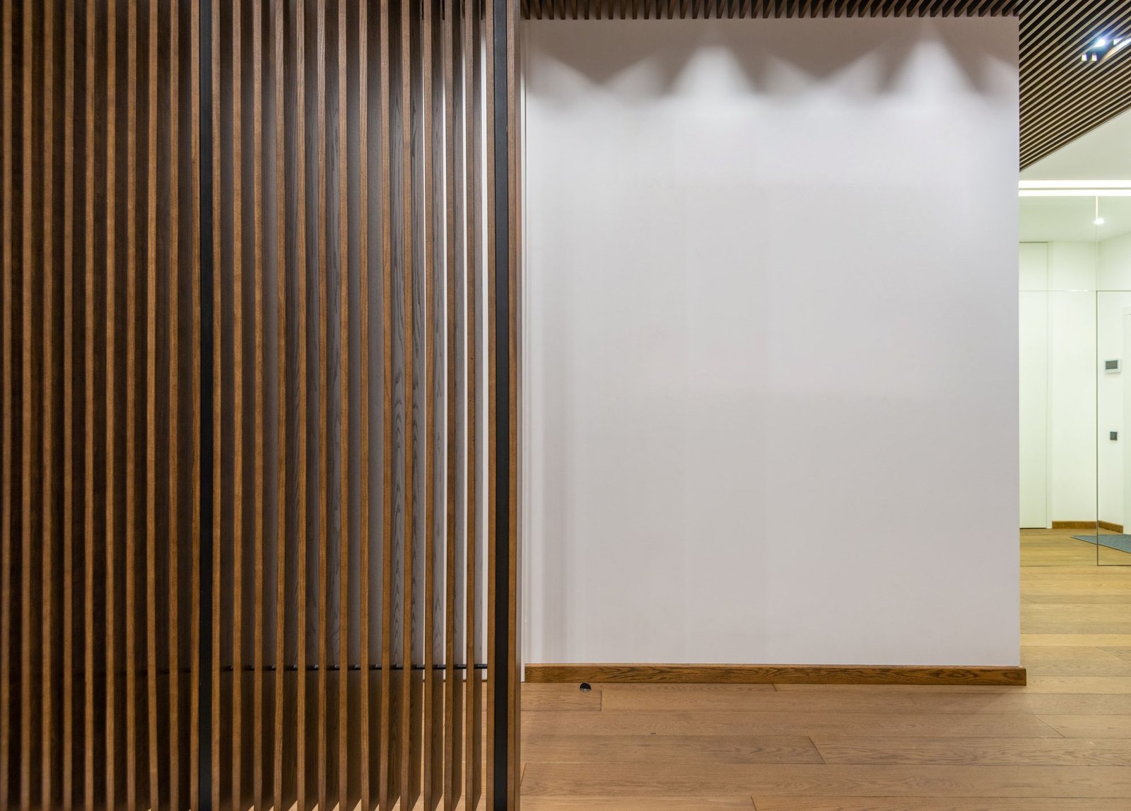 Thin decorative wooden slat partitions in a bright apartment corridor with white walls and parquet