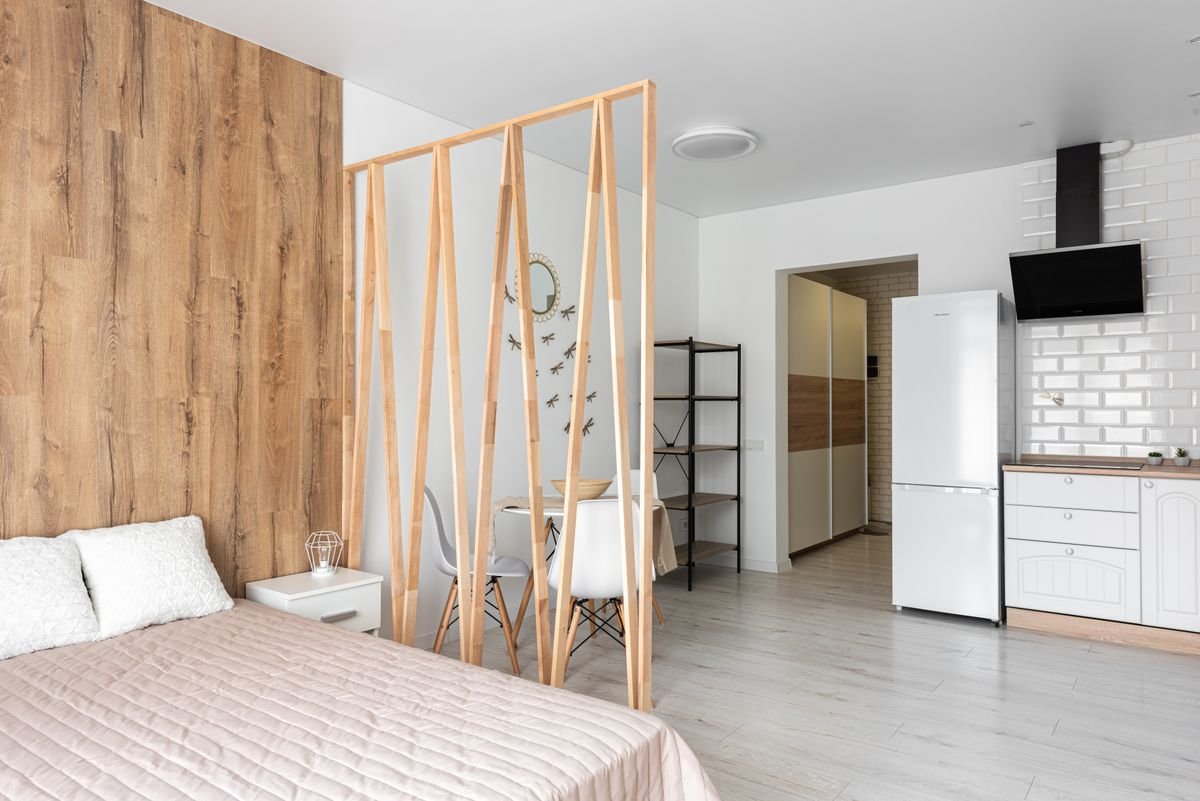 Bed with cushions beside a wooden partition screen and a compact kitchen