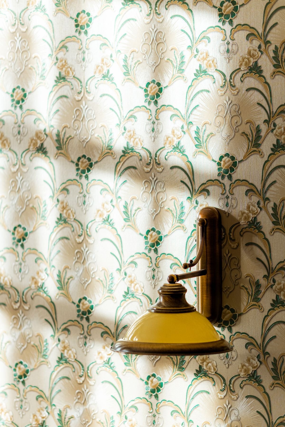 Embossed floral wallpaper catching raking light from a wall lamp