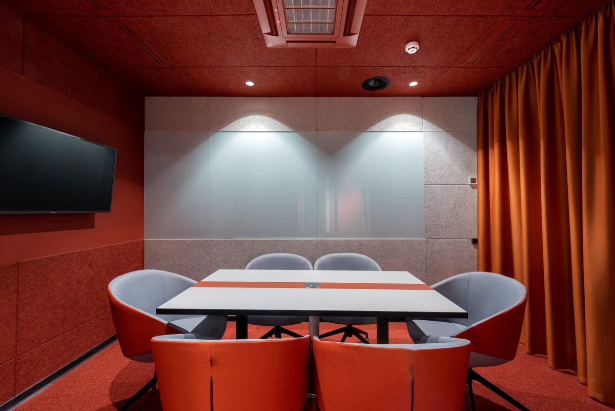 Meeting room with a red accent wall, wall-mounted TV, and orange curtain