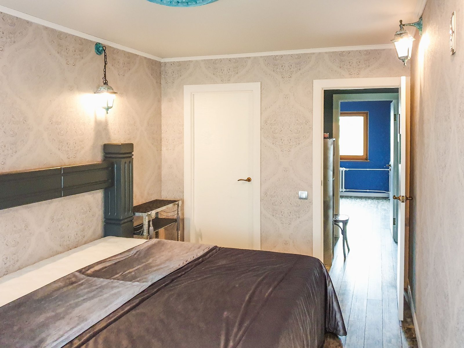 Bedroom walls covered in beige damask wallpaper with a white door and wall lamps