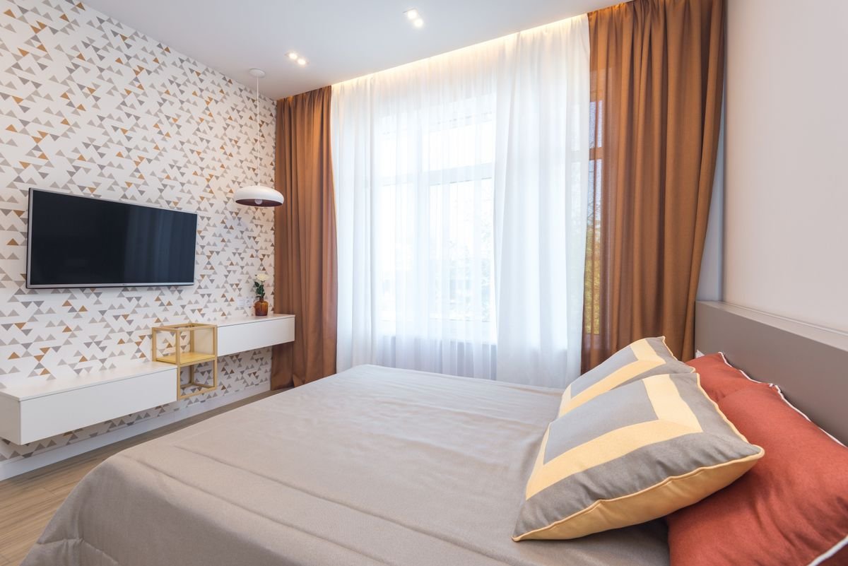 Bedroom with patterned wallpaper behind a wall-mounted TV beside heavy curtains