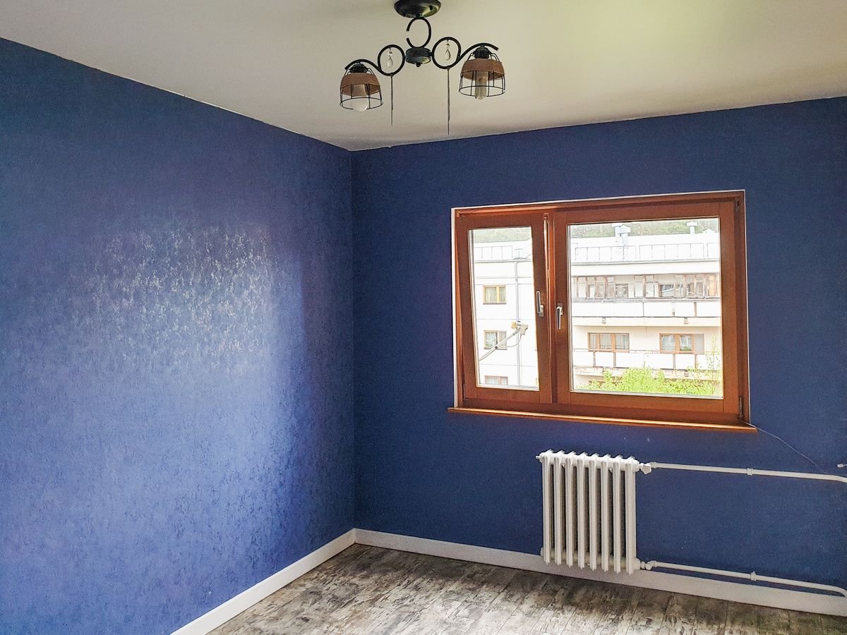 Room with deep blue textured wallpaper on every wall and a wooden window