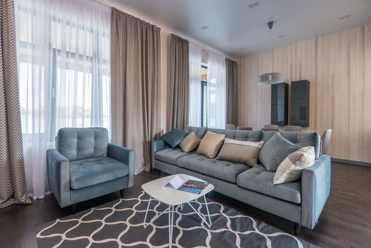Living room with smooth neutral walls, a grey sofa, and floor-to-ceiling curtains